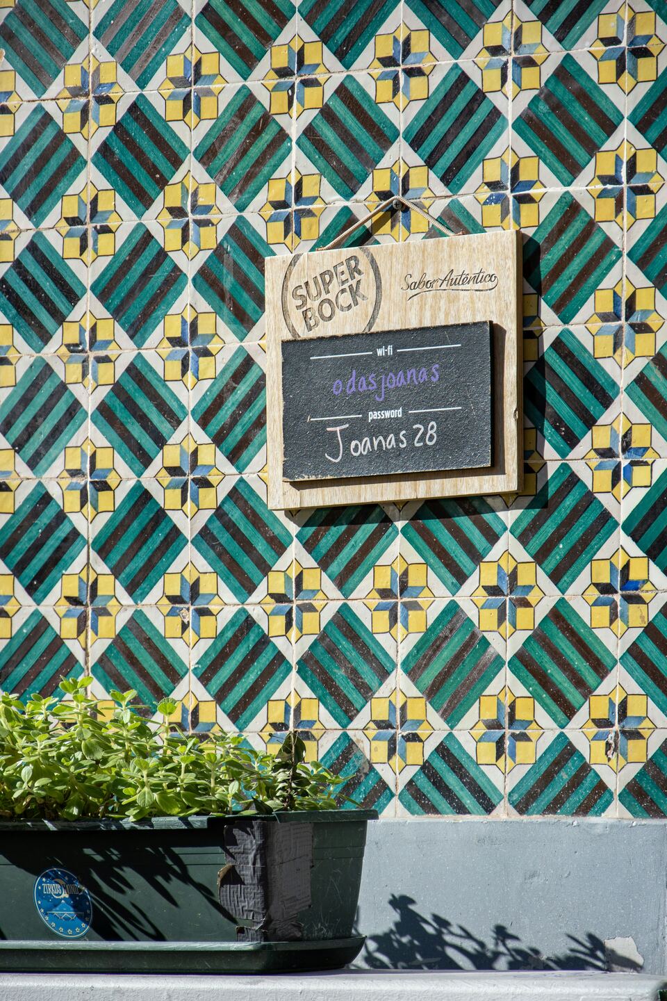 Parede de azulejos verdes e amarelos com uma pequena ardósia
