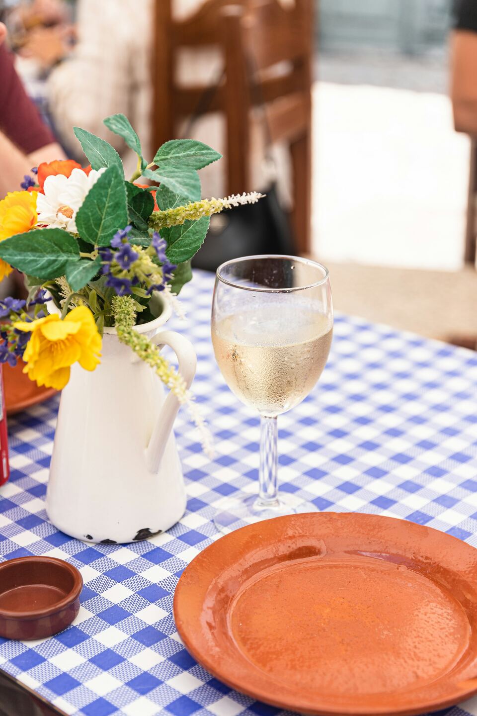 Mesa posta com toalha aos quadrados, flores do campo e um copo de vinho branco